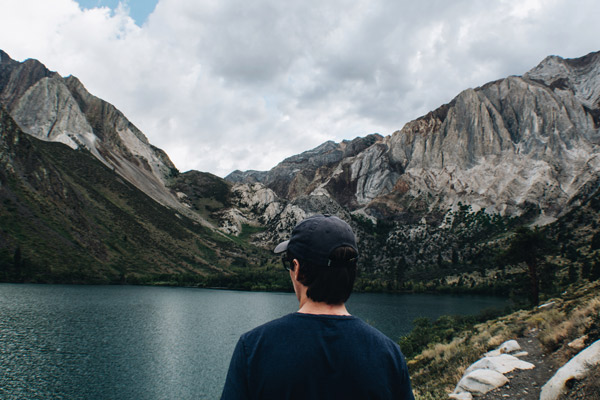 A man close up, wandering along a along that is framed all around by large, jutting mountains