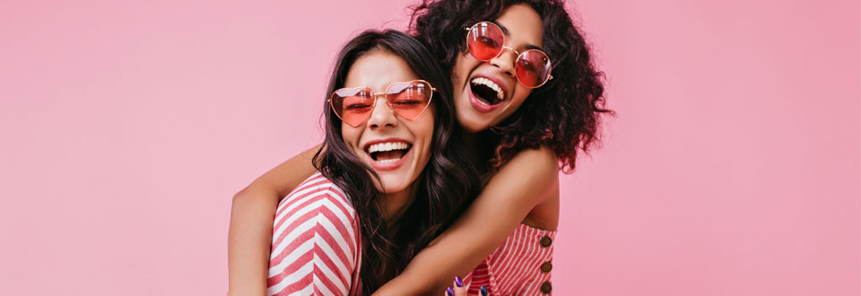 Two girls smiling big, wearing rose tinted sunglasses.