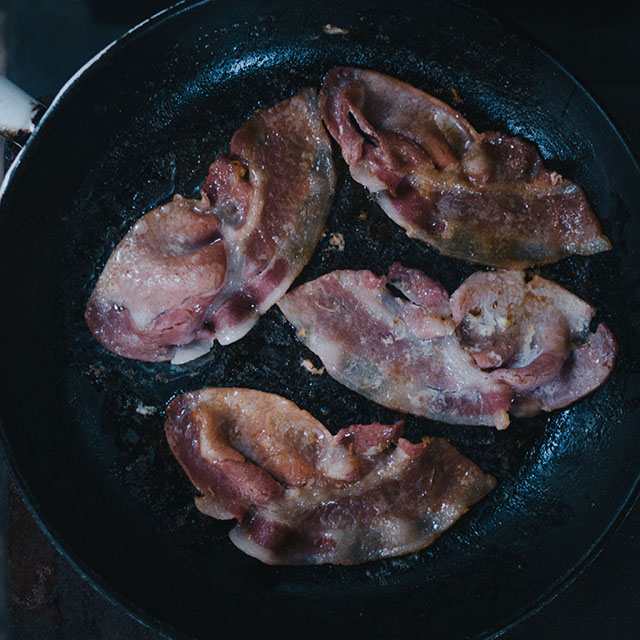 A pan with bacon cooking on it.