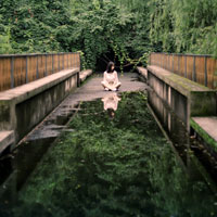 A woman sits at the end of the bridge with a reflecting pool of water.