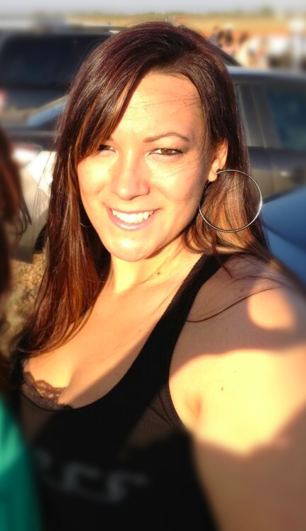 Close up image of a women standing outside with long brown hair, brown eyes, smiling.