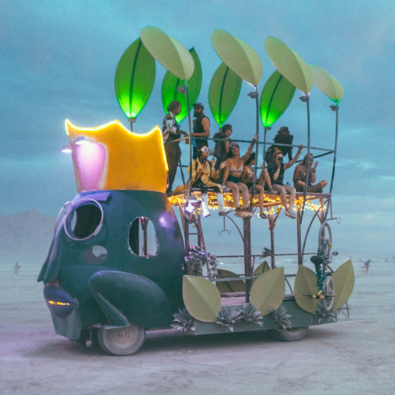 An art car of a frog prince with two decks of people sitting on it enjoying the view of the desert in the distance