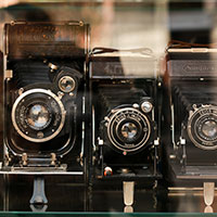 Three vintage cameras sitting side by side behind a window.