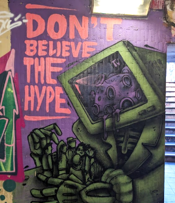A graffiti mural of a computer containing a covid virus, with the words 'Don't believe the hype'